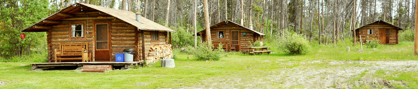 Three rustic log cabins sit among the trees.