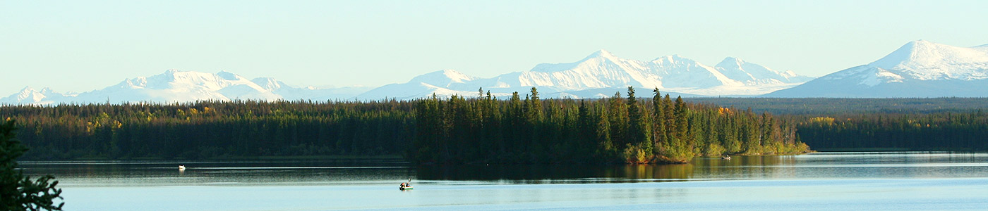 Three boaters can be seen out fishing on Nimpo Lake with snow covered mountains and autumn colored trees behind.