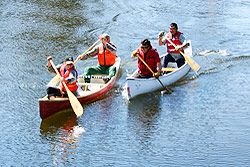 Four people in two canoes paddle madly next to each other.