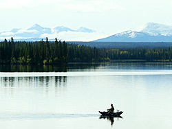 A man rows his pontoon boat across the water as he fishes.