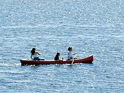 Three girls paddle a canoe across water that glints like diamonds.