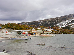 Two planes parked on shore of a high wilderness lake.