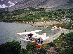 People with a canoe and airplane on the shore of a high alpine lake.