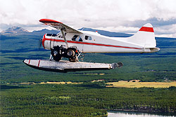 A floatplane has an ATV strapped to the float high above surrounding land. 