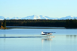A black and white plane on the lake with snowcovered mountains behind.