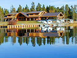 Two white planes moored in front of log lodge with reflection in the dark blue water.