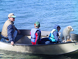 Two kids, an adult and a dog go out fishing in a boat.
