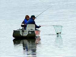 A woman and man pull in a net with a rainbow trout in it.