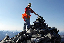 Photo courtesy of Ed Wilson. Man standing atop rock cairn on a mountain peak.