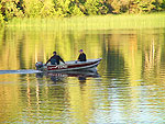 Two men in a motorboat go out on Nimpo Lake with trees reflected in the water.